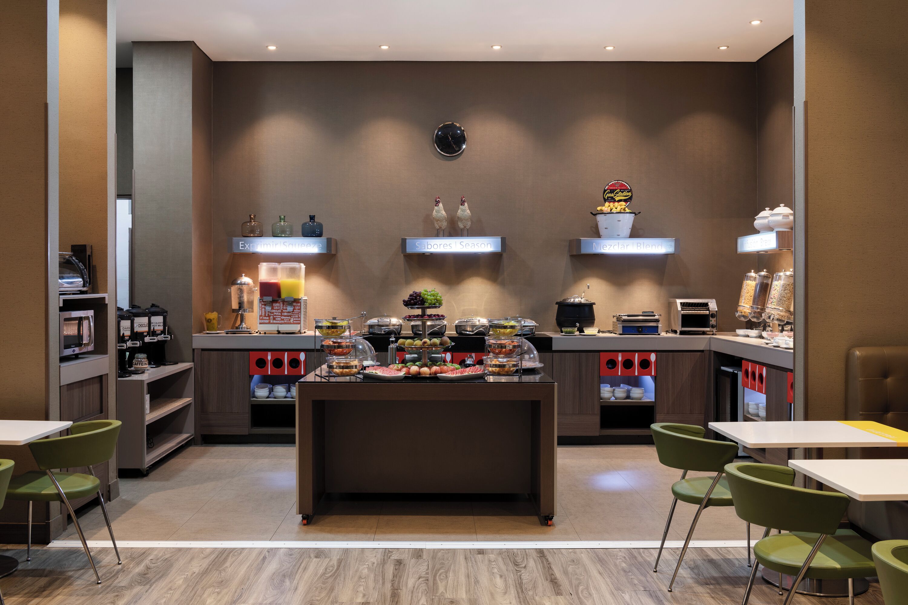 Un espace moderne dédié au petit-déjeuner, avec une table de buffet centrale, des chaises vertes et une horloge au mur.