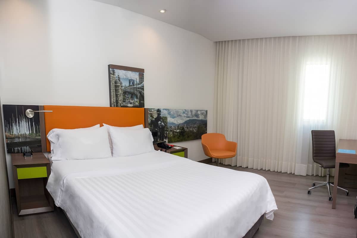 A hotel room with a bed, a desk with a computer, a chair, and a TV.