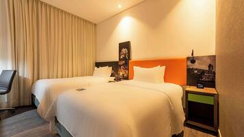 A hotel room with two beds, a chair, a nightstand with a clock, and a wall-mounted picture.