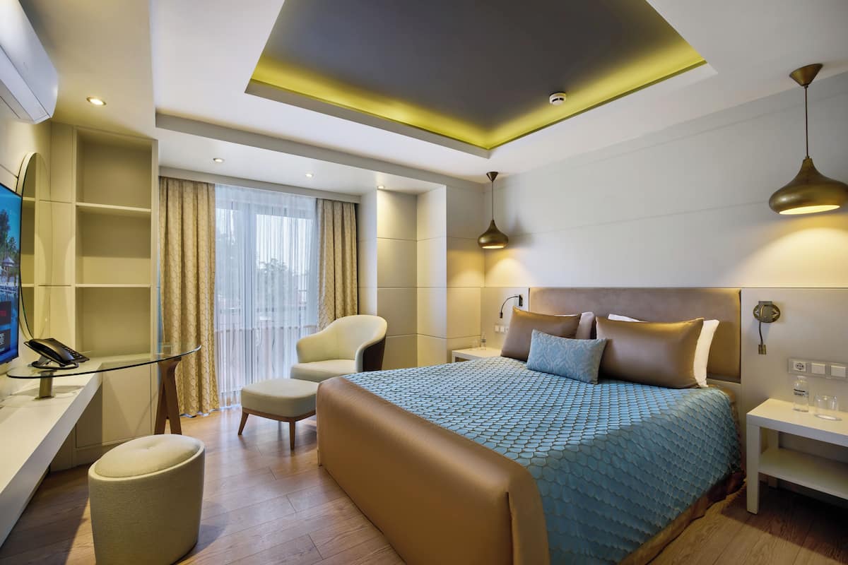 A modern hotel room with a large bed, a desk with a telephone, a chair, and a small ottoman.