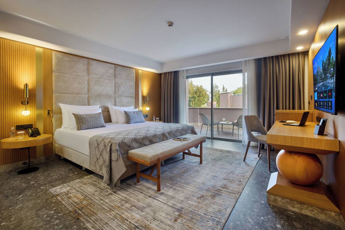 A modern hotel room with a large bed, a desk, a laptop, and a television.