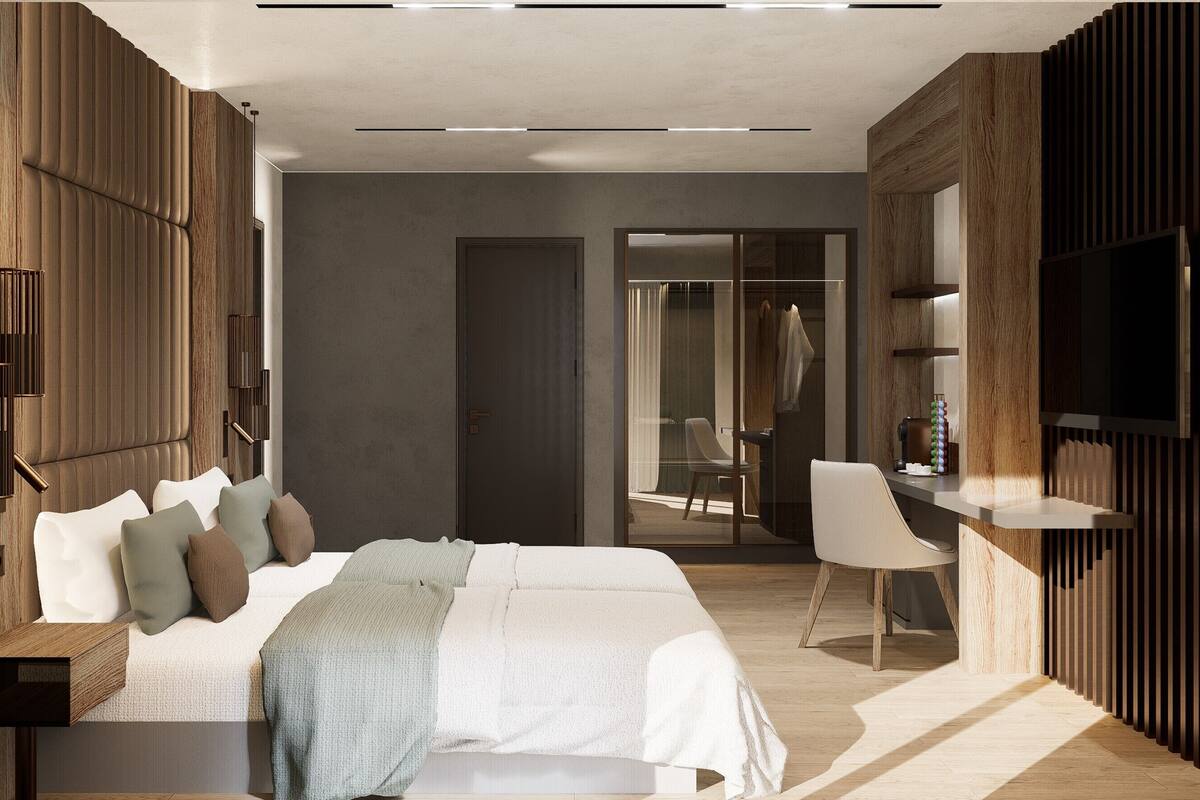 A modern hotel room with a large bed, a TV, a desk, and a bathroom visible through a glass door.