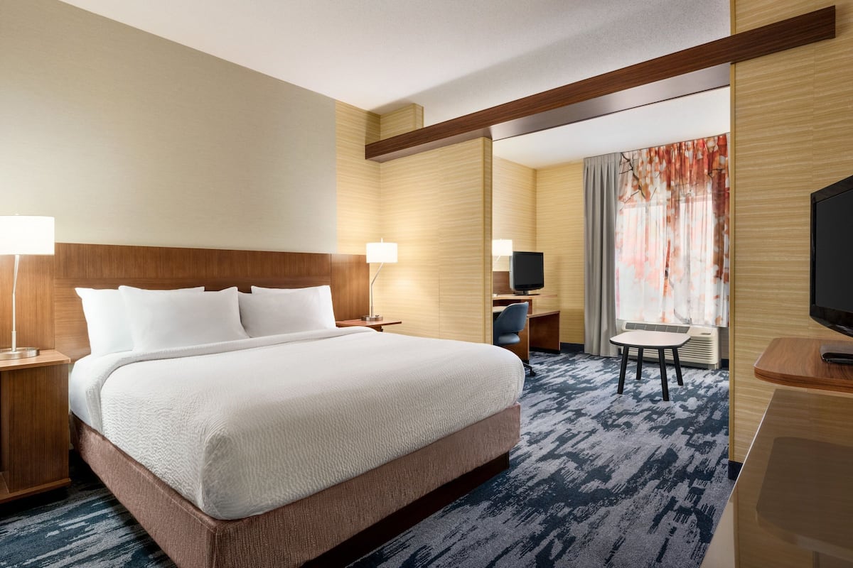 Ein Hotelzimmer mit einem großen Bett, einem Schreibtisch mit Stuhl, einem Fernseher und einem Fenster mit Vorhängen.