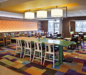Um saguão de hotel com área de bar central, diversas opções de assento incluindo cabines e mesas, e carpete estampado.
