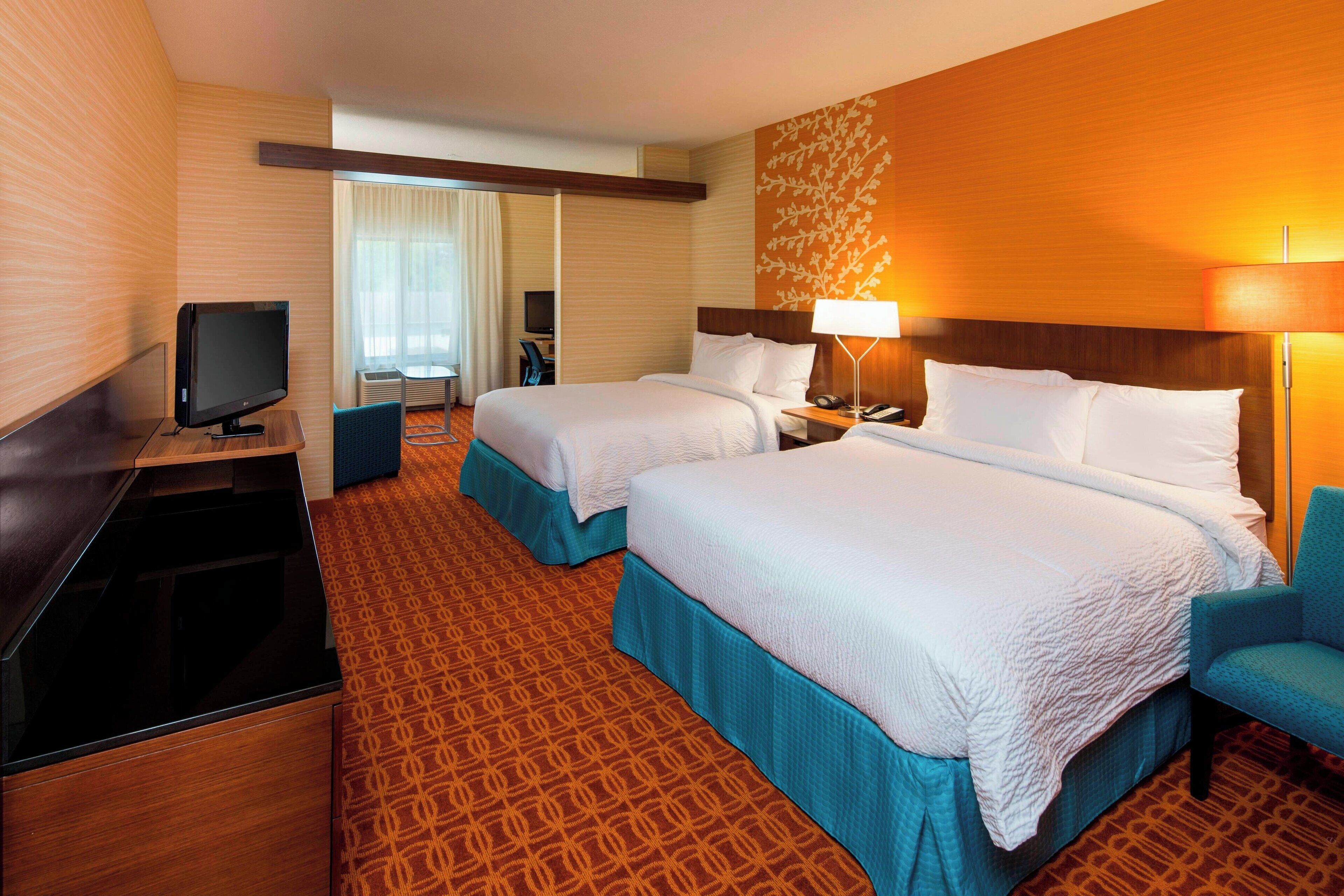 A hotel room with two beds, a television, a desk, and a chair.