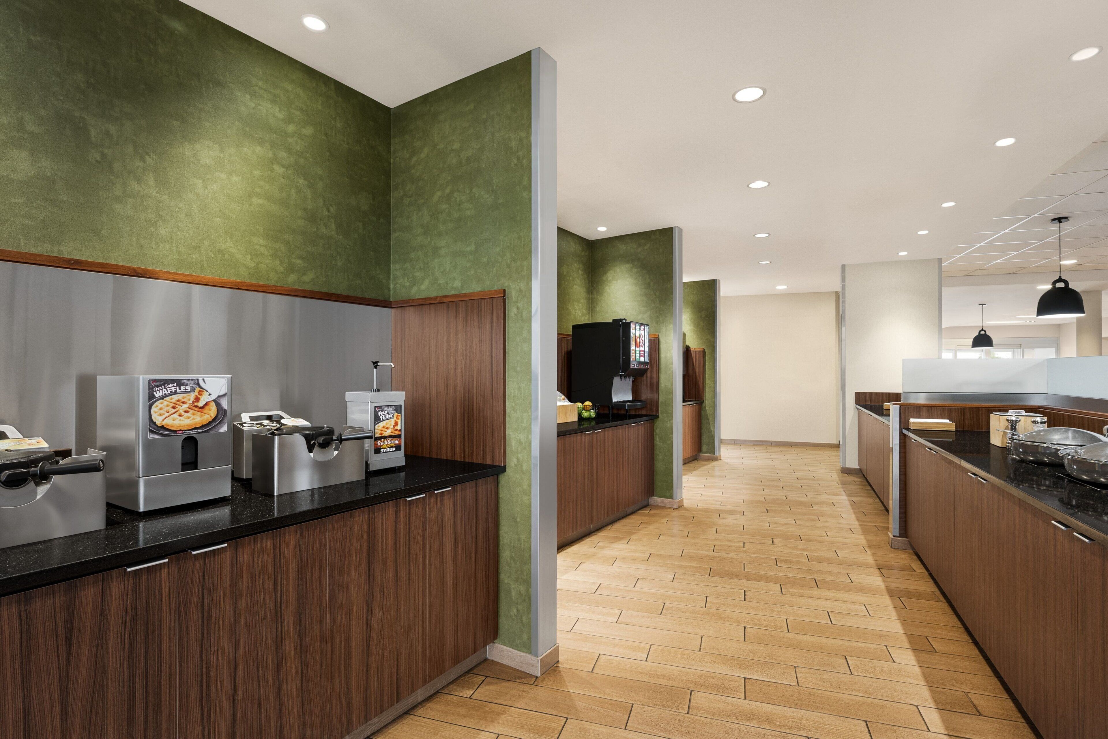 A modern kitchen with a waffle maker, coffee machine, and a refrigerator.