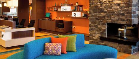 A modern hotel lobby with a blue sofa, a fireplace, and a reception desk.