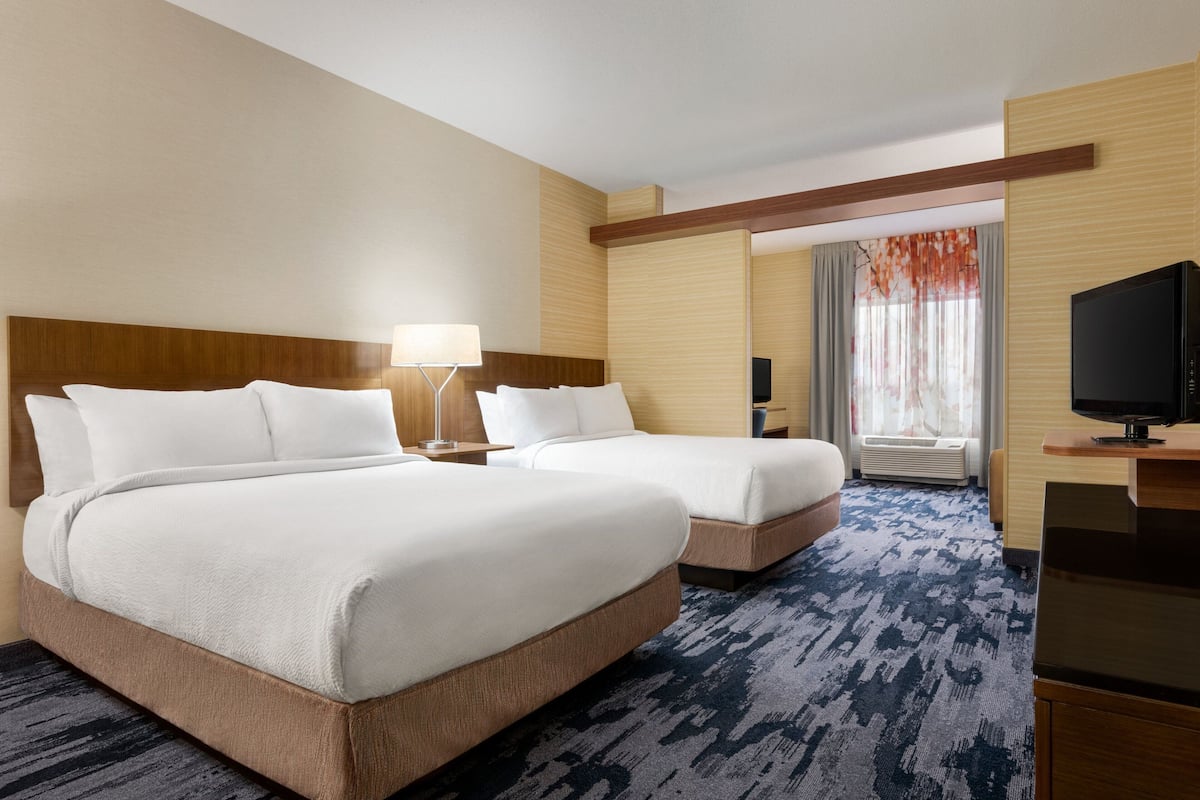 Ein Hotelzimmer mit zwei Betten, einem Fernseher, einem Schreibtisch und einem Fenster mit Vorhängen.