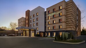 Ein mehrgeschossiges Hotel mit modernem Design, das einen markanten Eingangsbereich mit einem überdachten Gang und ein Parkfeld davor aufweist.