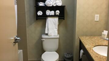 A bathroom with a toilet, a towel rack with towels, a sink, and a trash can.