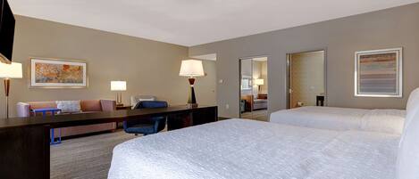 A hotel room with a large bed, a desk, a chair, a sofa, and two lamps.