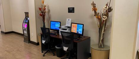 Un centro de negocios con dos estaciones de trabajo por computadora, un mostrador de recepción y un quiosco de auto servicio.