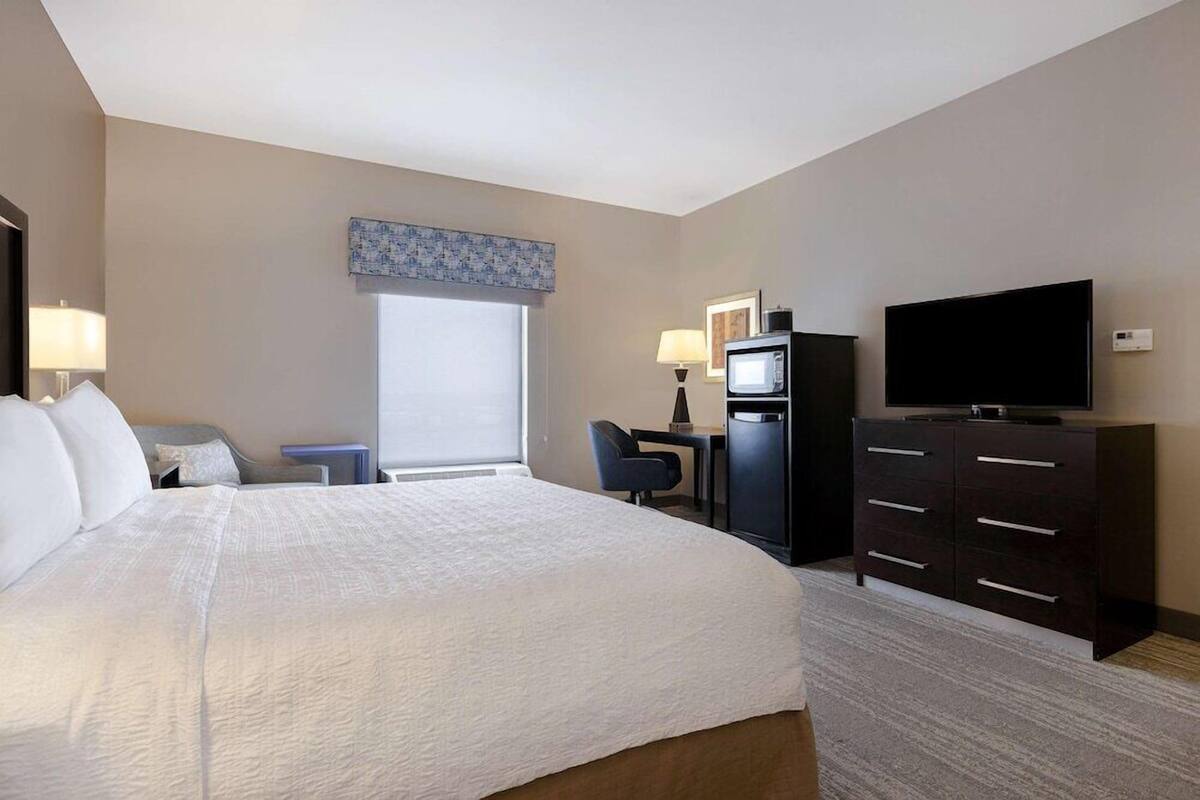 A hotel room with a large bed, a desk, a television, and a dresser.