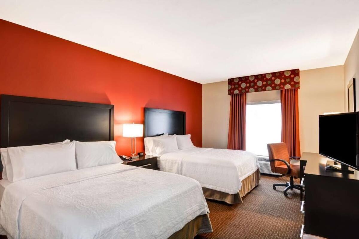 Une chambre d’hôtel avec deux lits, un bureau, une télévision et une fenêtre avec des rideaux.