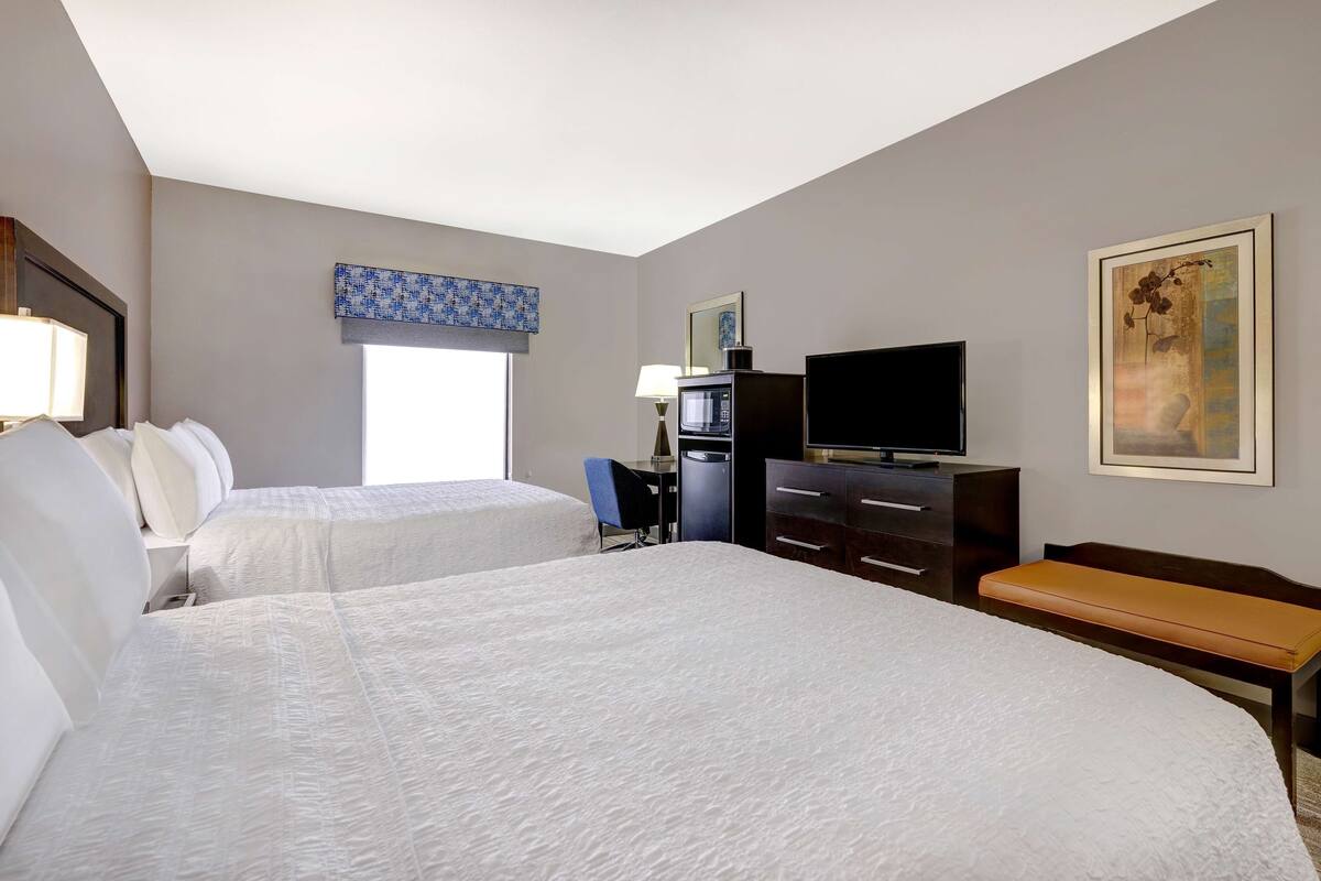 A hotel room with two beds, a desk, a television, and a painting on the wall.