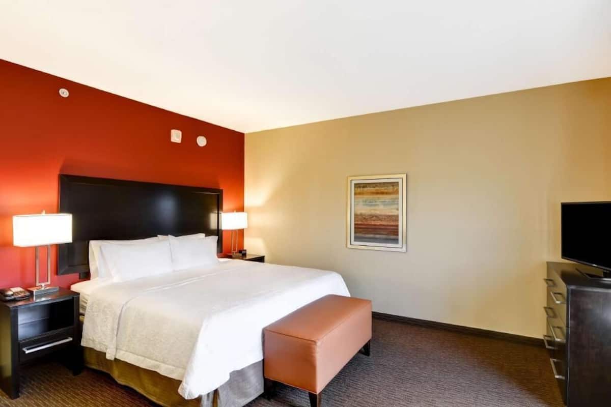 Une chambre d’hôtel avec un lit, une table de chevet, une lampe, un téléviseur, un banc et un tableau au mur.
