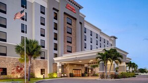 Ein Hotel mit freiem Zugang, einer Schilder mit der Aufschrift "Hampton Inn & Suites" und einer Fahnenstange mit der US-Flagge.