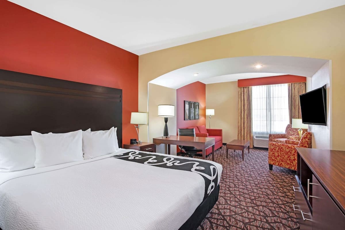 Une chambre d’hôtel avec un grand lit, un bureau, une chaise, une télévision et une fenêtre avec des rideaux.