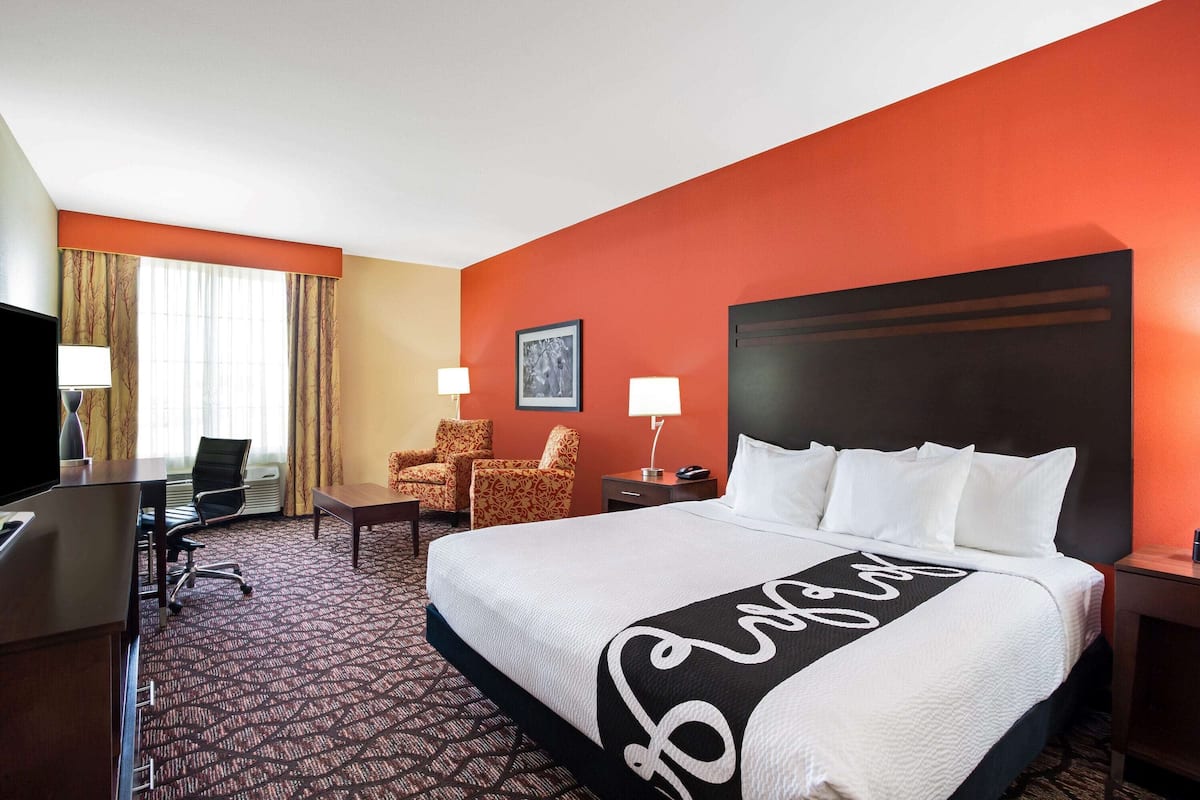 Une chambre d’hôtel avec un grand lit, deux fauteuils, un bureau et un téléviseur.
