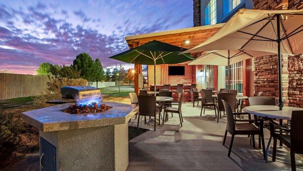 An outdoor patio area with a stone fire feature, tables, chairs, and umbrellas. - La Quinta Inn & Suites by Wyndham Pecos (Pecos)