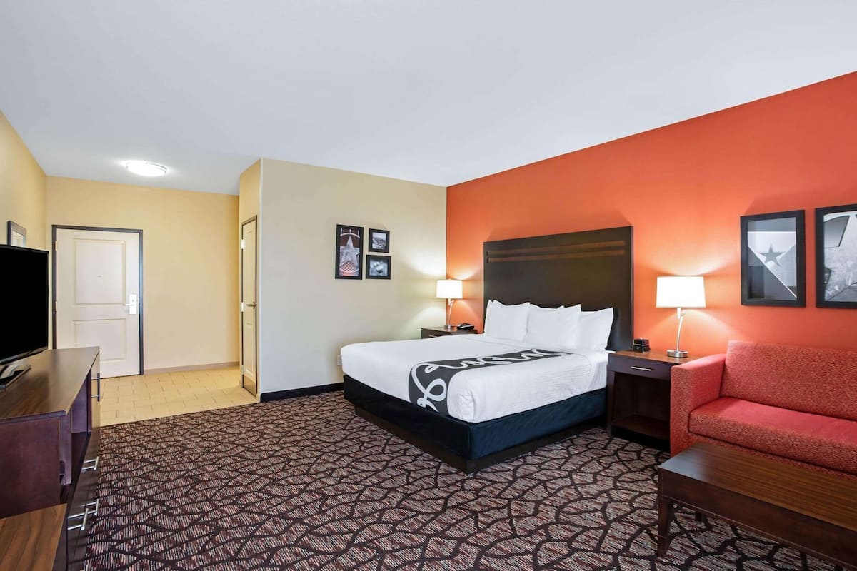 Une chambre d’hôtel avec un lit, une télévision, un canapé rouge et une moquette à motifs.