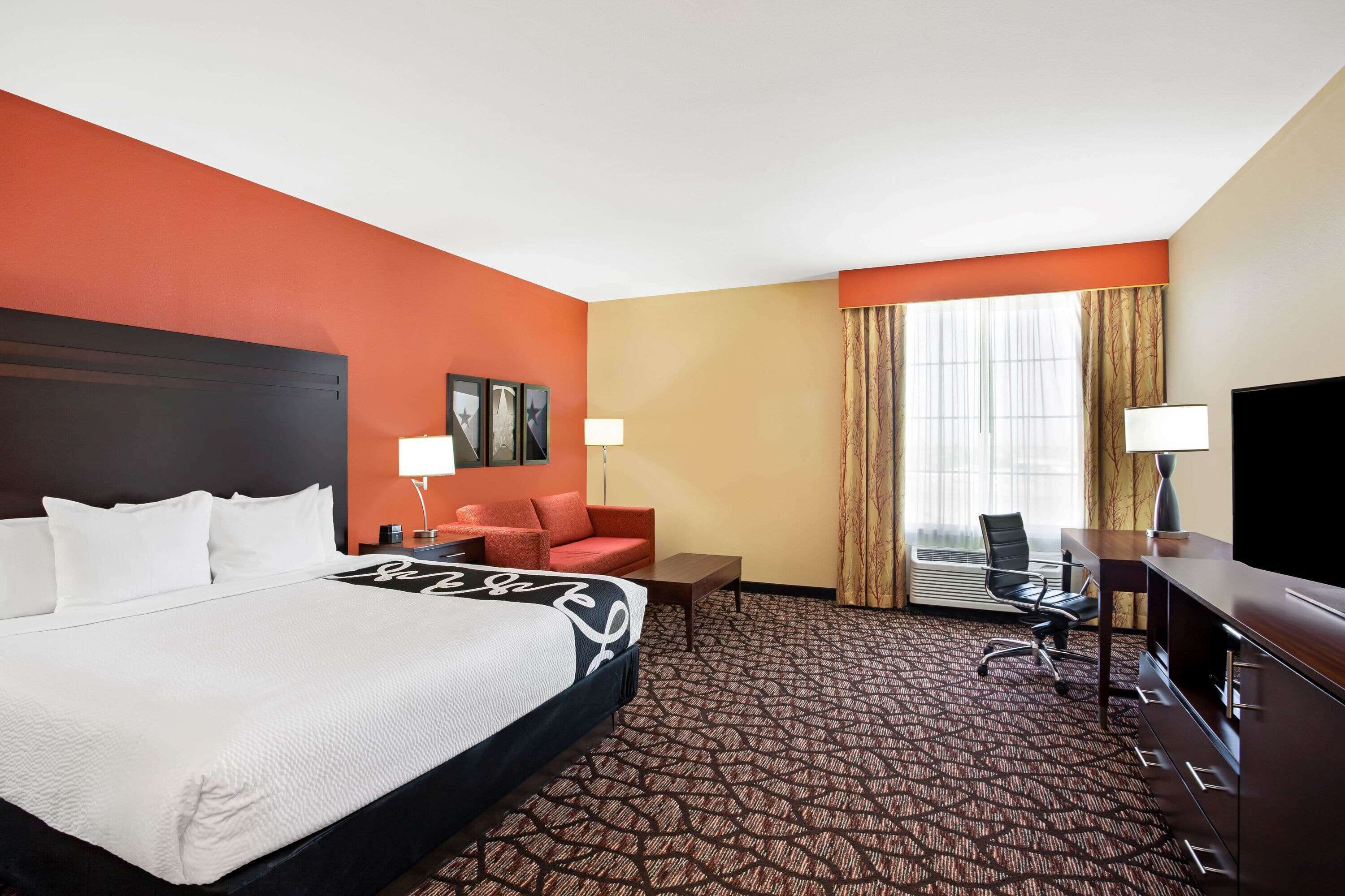 A hotel room with a large bed, a desk, a chair, a TV, and a window with curtains.