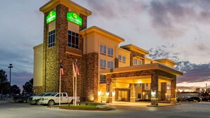A hotel with a stone facade, a prominent tower with signage, and a well-lit entrance. - La Quinta Inn & Suites by Wyndham Pecos (Pecos)