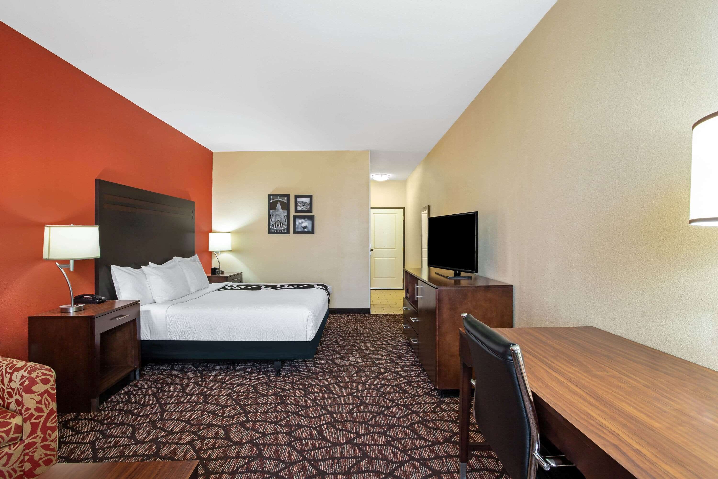Una habitación de hotel con cama, escritorio, silla, televisor y lámpara.