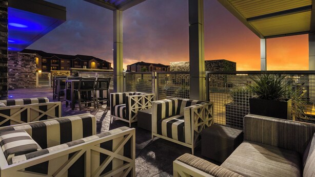 An outdoor seating area with striped sofas and chairs, a stone wall, and a view of buildings in the background. - SpringHill Suites by Marriott Midland Odessa (Midland)