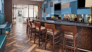 A modern bar area with wooden bar stools, a counter with a variety of bottles, and a television mounted above the bar. - SpringHill Suites by Marriott Midland Odessa (Midland)