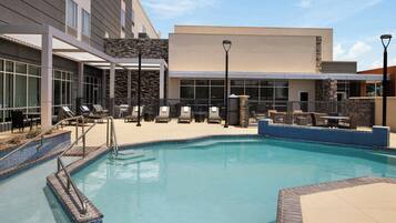 A swimming pool area with lounge chairs and a building with large windows and a stone facade.