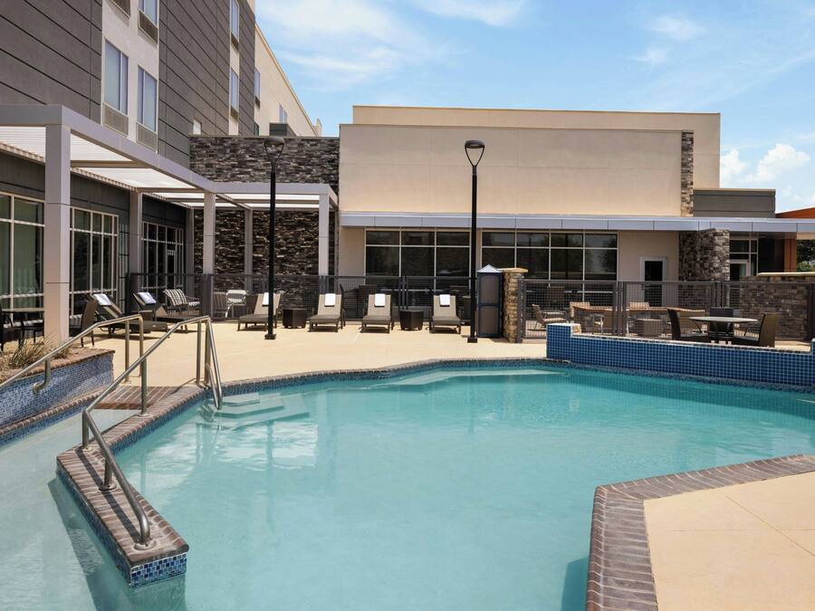 A swimming pool area with lounge chairs and a building with large windows and a stone facade.