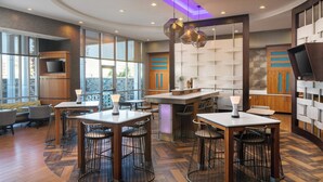 A modern restaurant with high tables, bar stools, and a large TV screen. - SpringHill Suites by Marriott Midland Odessa (Midland)