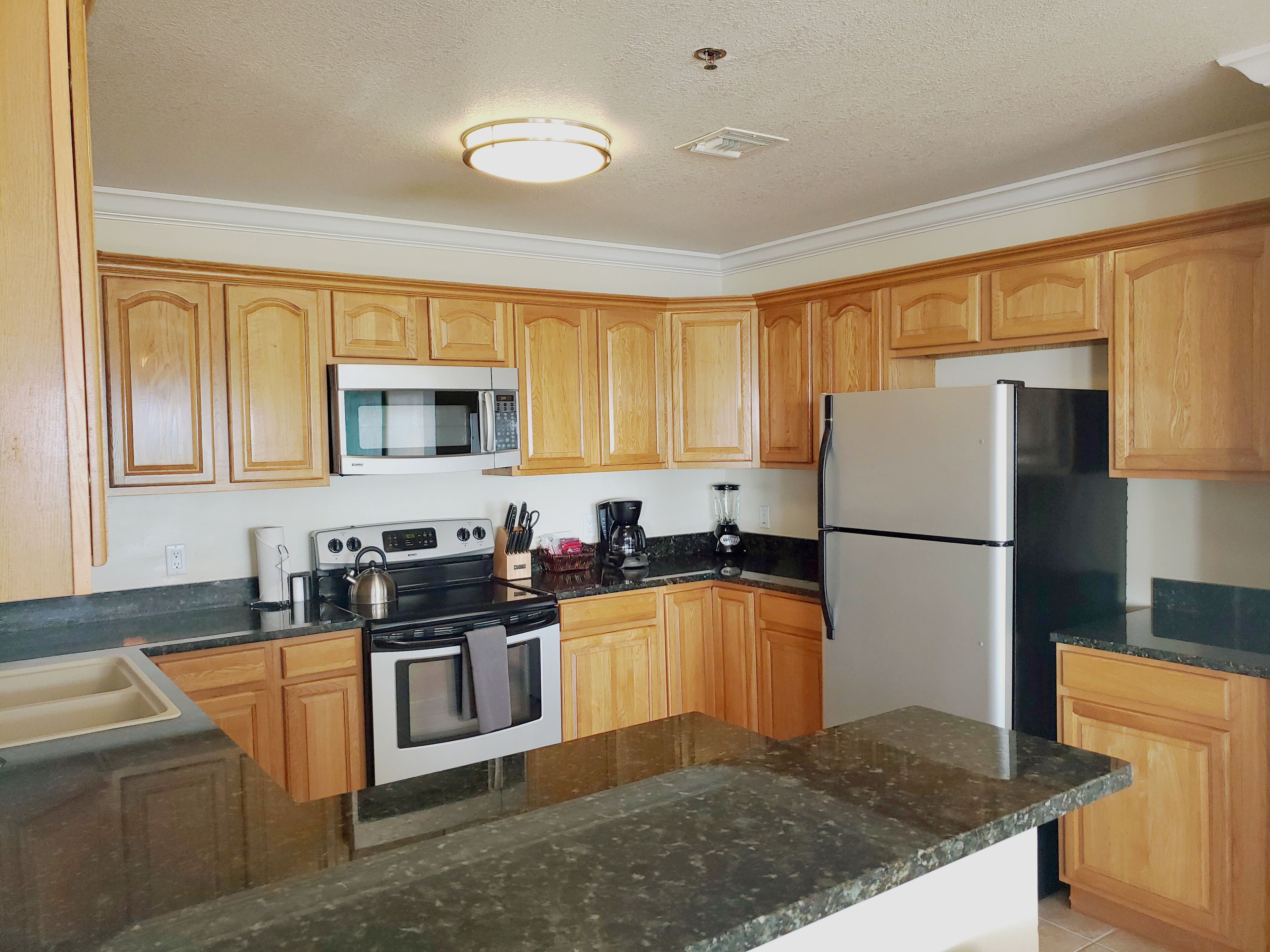 A kitchen with wooden cabinets, a microwave, stove, refrigerator, and granite countertops.