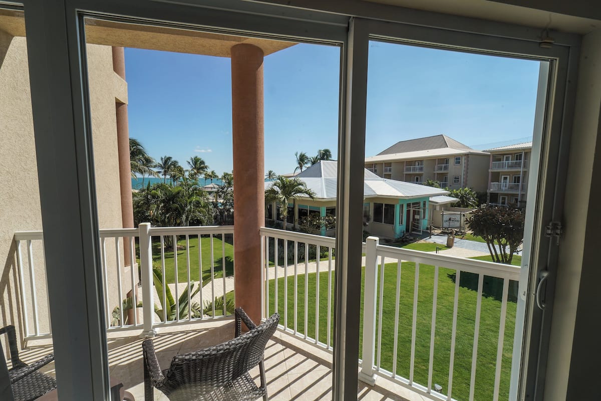 A balcony with wicker chairs, a white railing, and a view of a well-maintained lawn and buildings in the background.