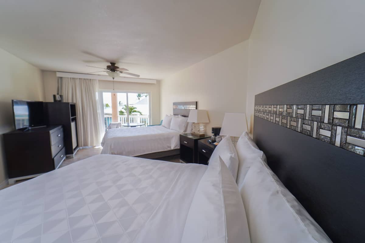 A hotel room with two beds, a ceiling fan, a TV, a desk with a lamp, and a view of the outdoors.
