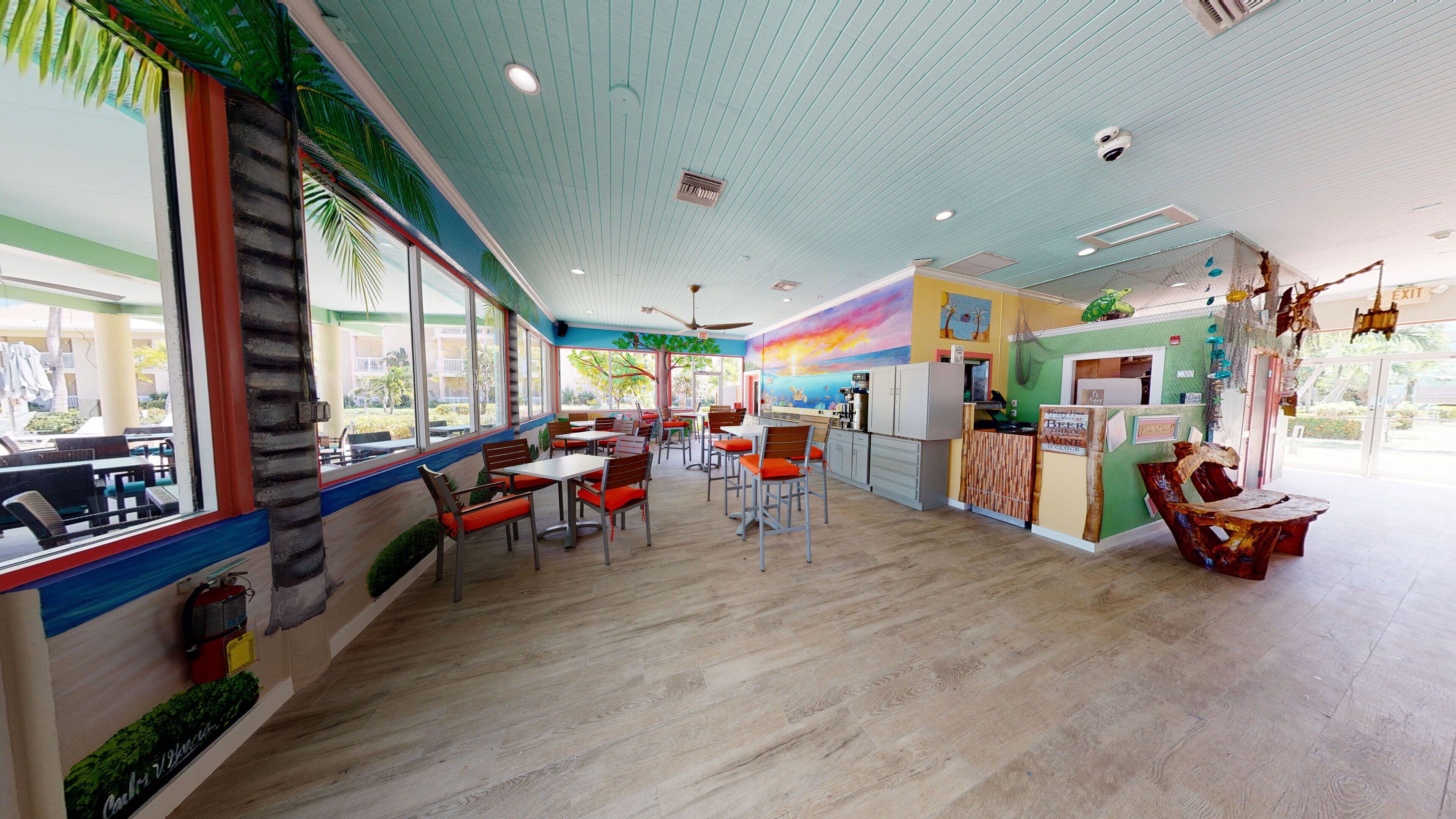 Un restaurante con piso de madera, mesas con cojines anaranjados y un mural en la pared.