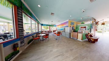 Un restaurante con piso de madera, mesas con cojines anaranjados y un mural en la pared.