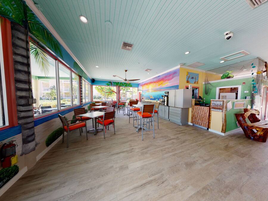 Un restaurante con piso de madera, mesas con cojines anaranjados y un mural en la pared.