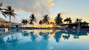 A clear swimming pool with palm trees and a sunset in the background. - Holiday Inn Resort Grand Cayman by IHG (West Bay)