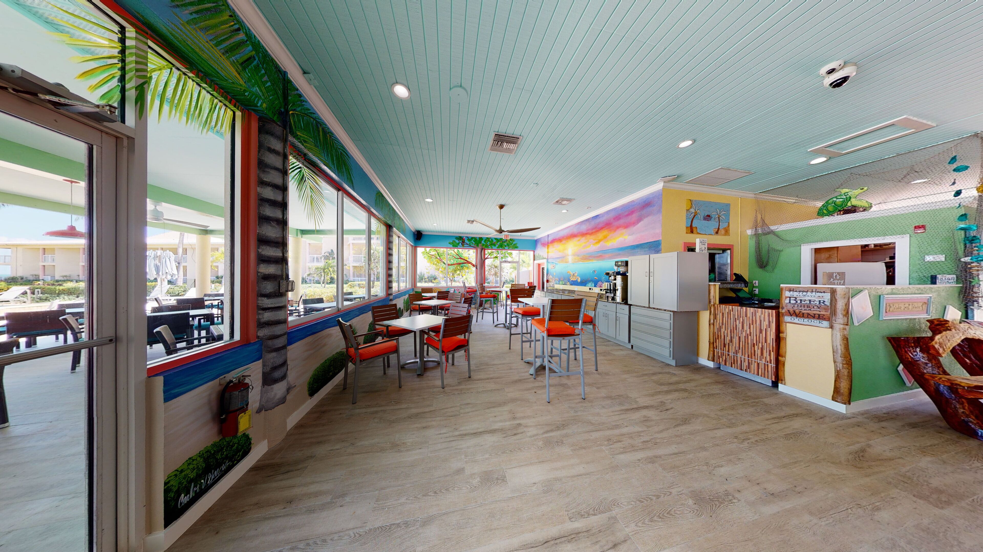A restaurant with a wooden floor, large windows, and a colorful mural on the wall.
