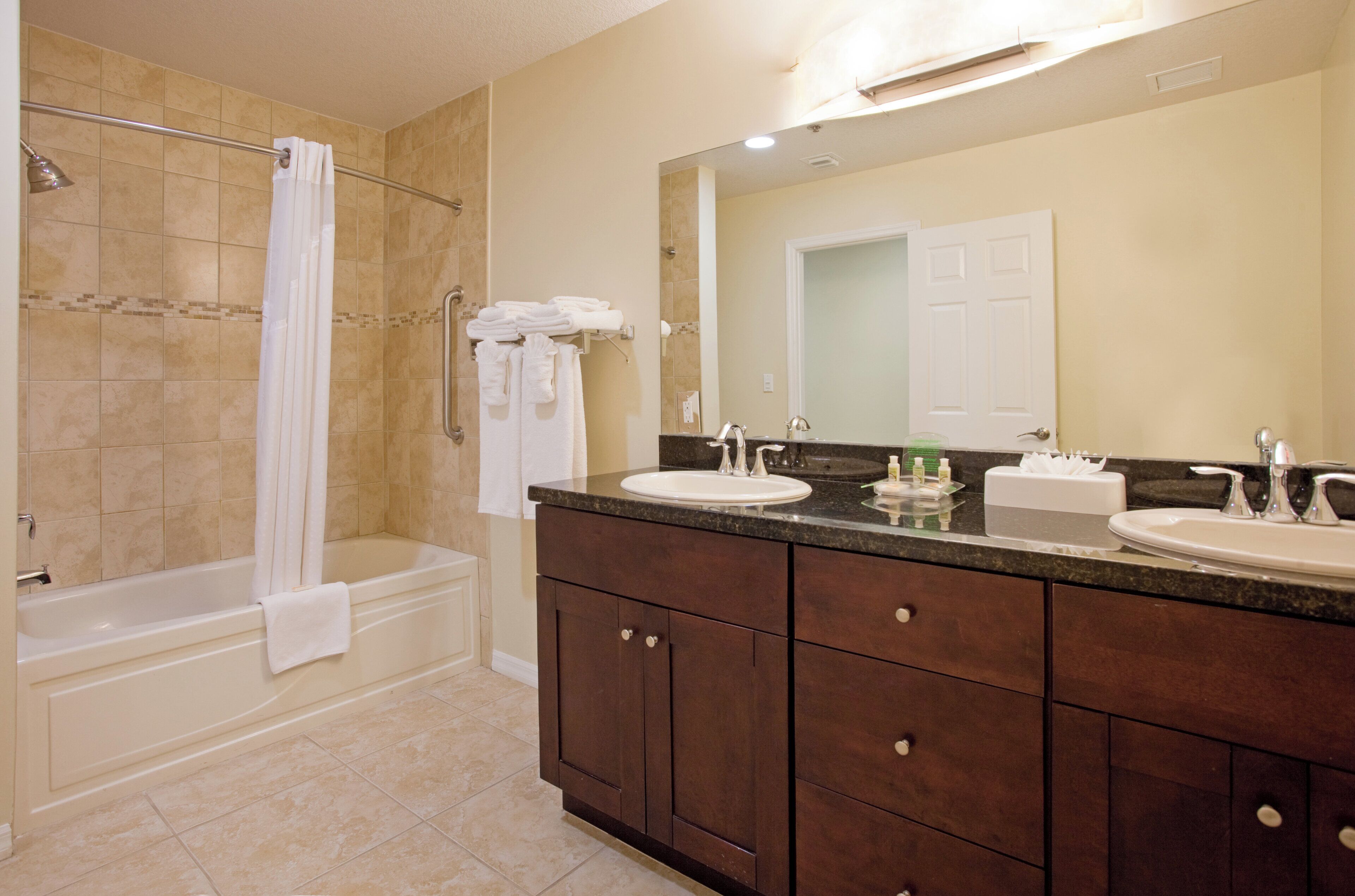 A bathroom with a bathtub, two sinks, a vanity with cabinets, and a large mirror.