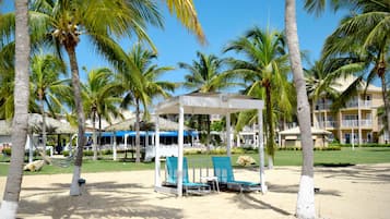 A beach area with palm trees, a covered seating area, and a building with balconies.