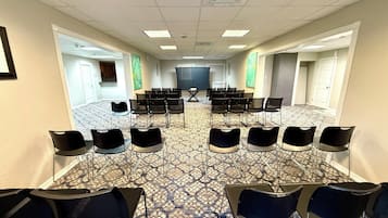 Un salón de conferencias con filas de sillas, una pantalla de proyector y una alfombra estampada.