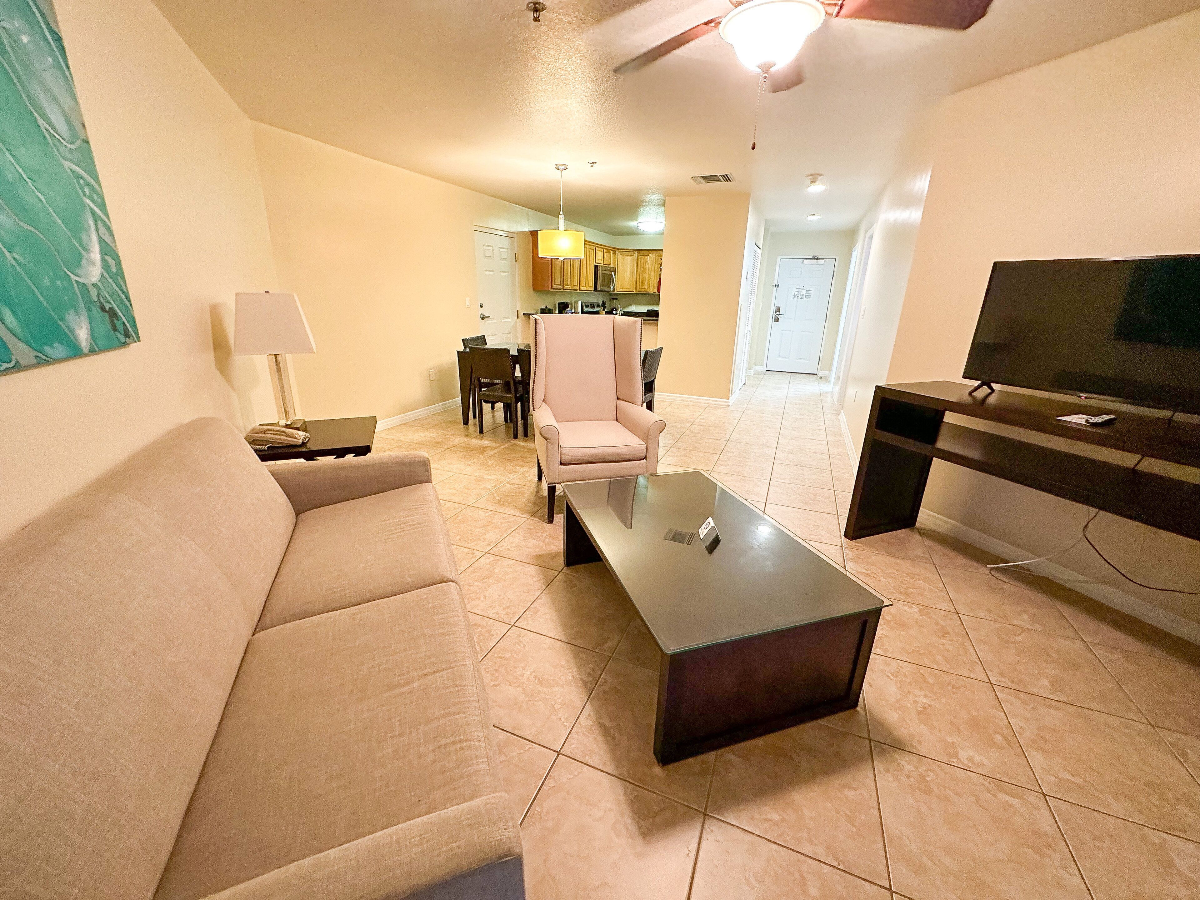 A living room with a sofa, a coffee table, a TV, and a dining area in the background.