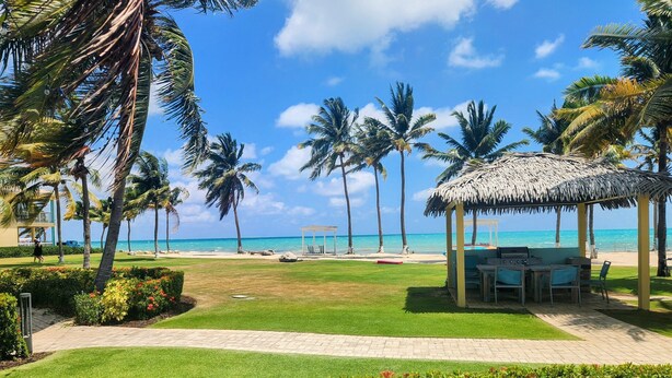 A beachside resort with a thatched gazebo, palm trees, and a clear view of the ocean. - Holiday Inn Resort Grand Cayman by IHG (West Bay)