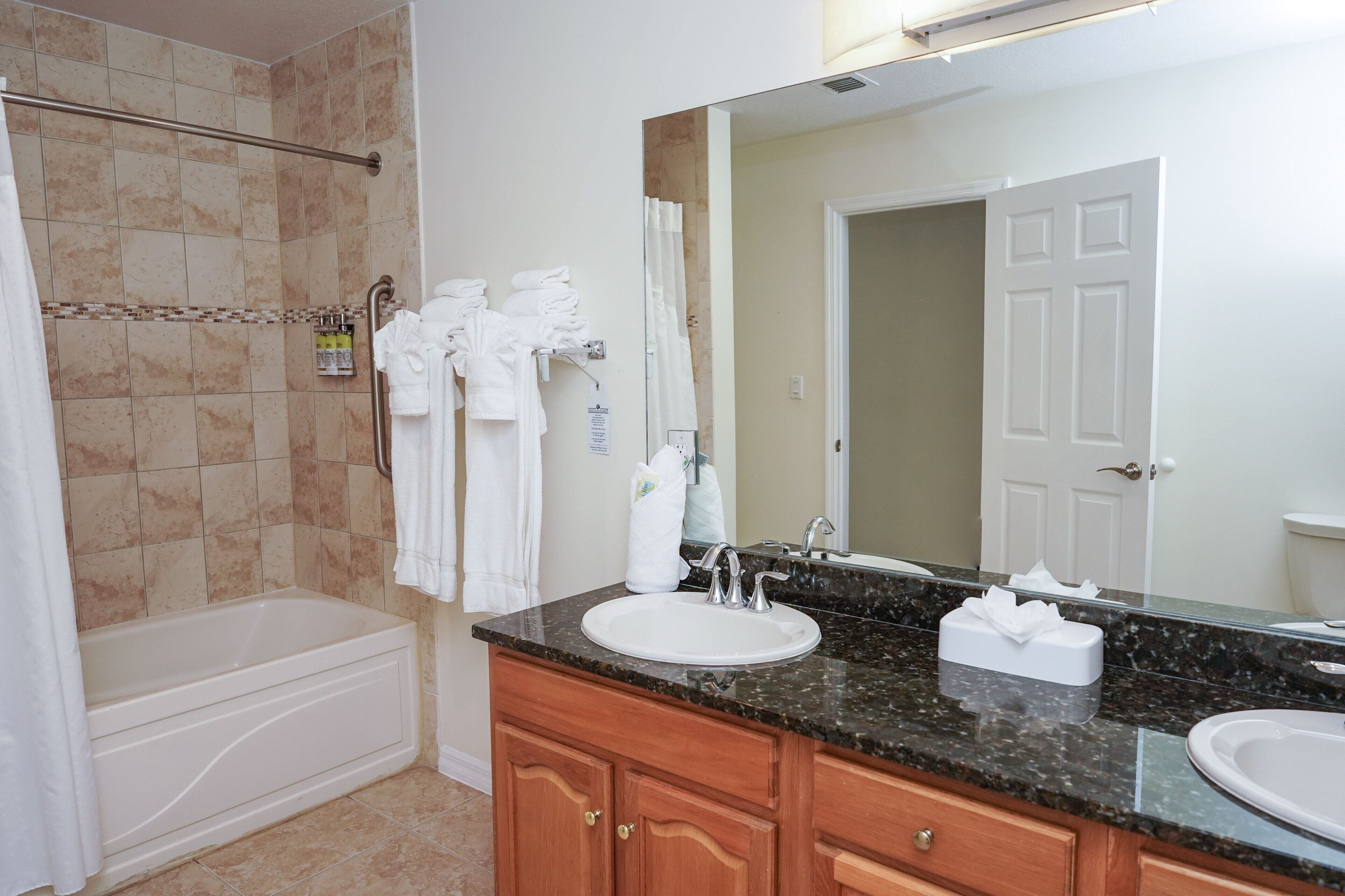 A bathroom with a bathtub, two sinks, a large mirror, and towels hanging on a rack.