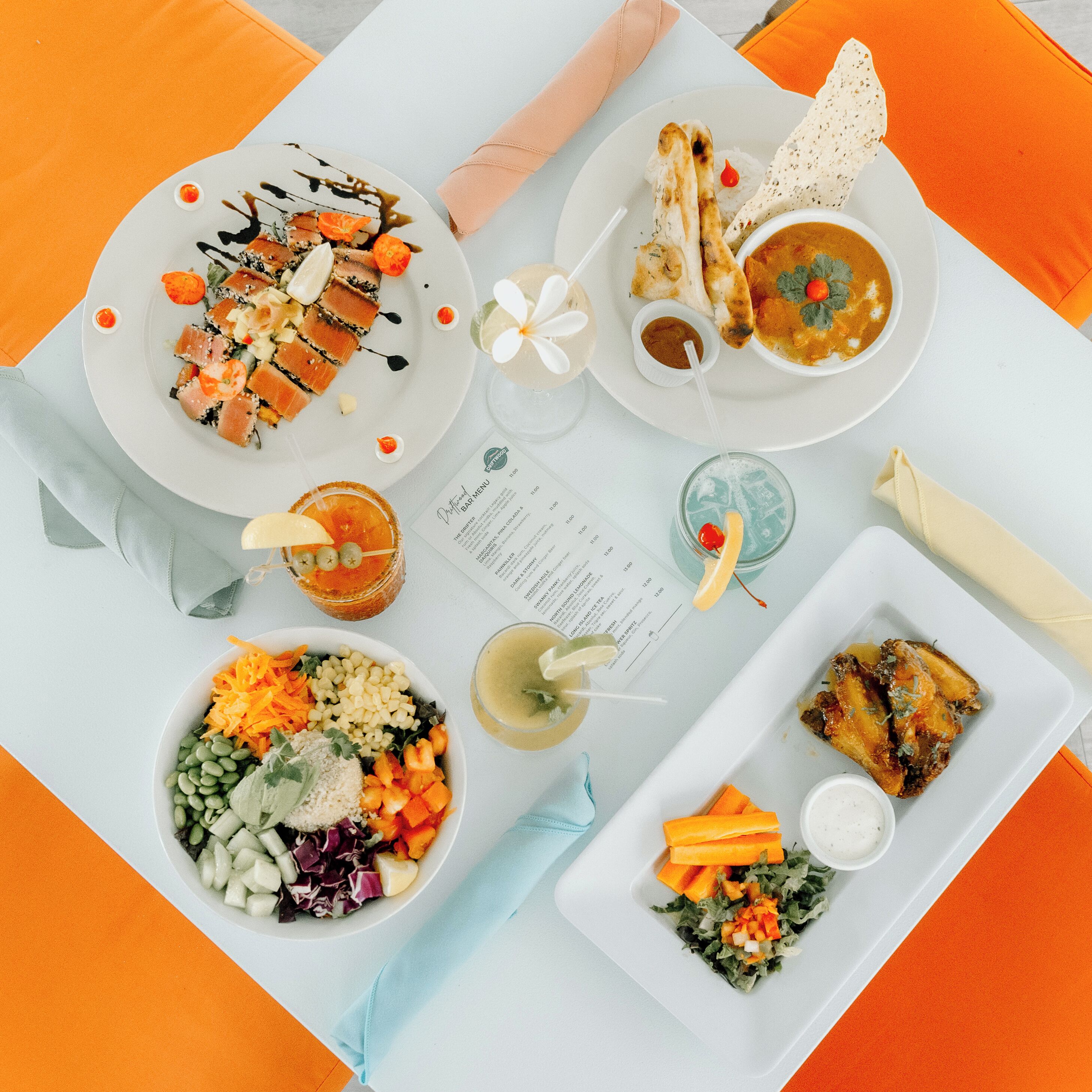 A table with various dishes including sushi, soup, and a salad, along with a menu and drinks.