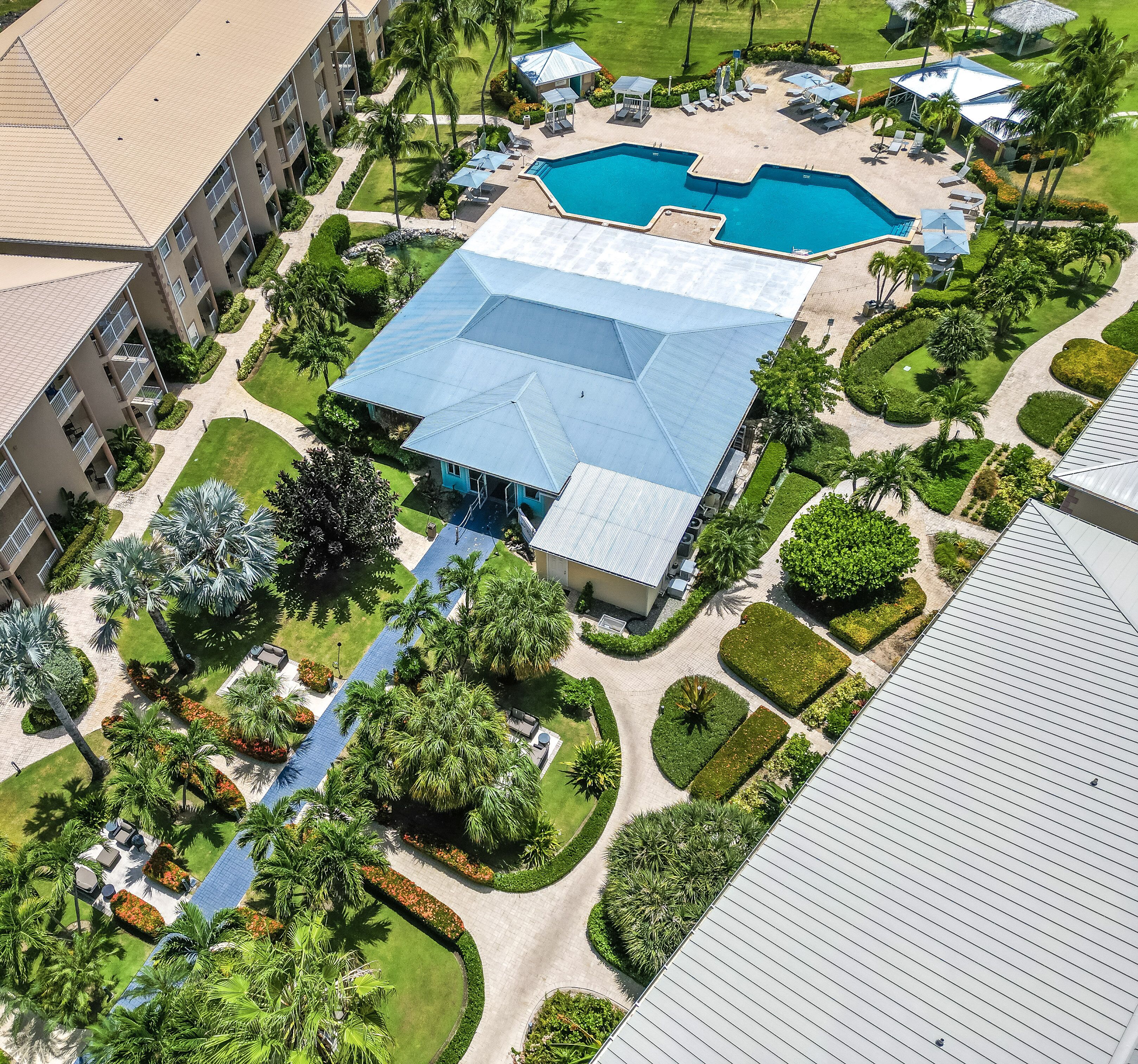 An aerial view of a resort with a swimming pool, landscaped gardens, and a large building with a blue roof.