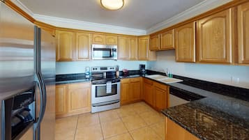 Una cocina con armarios de madera, un refrigerador de acero inoxidable, un microondas, un horno y un lavamanos.